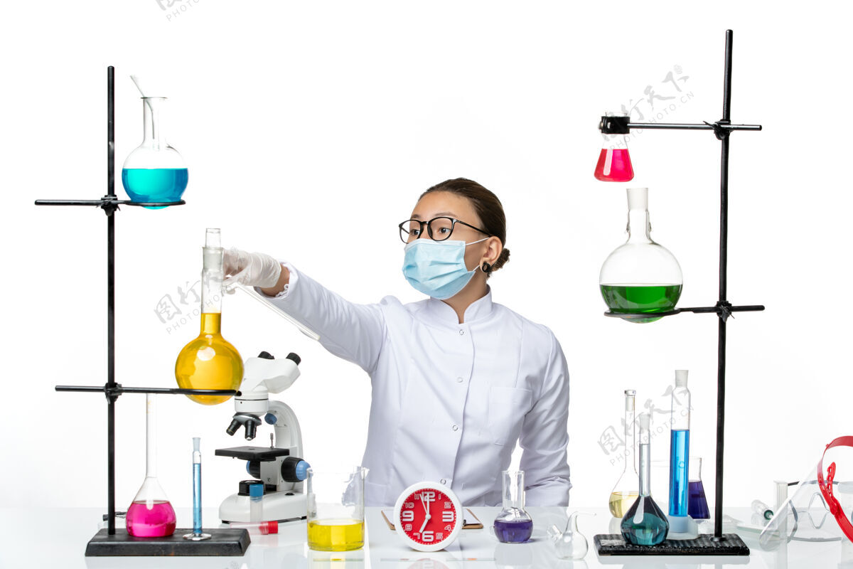 化学前视图：穿着医疗服的女化学家戴着面罩 坐在浅白背景上的溶液化学实验室病毒-喷溅化学套装喷溅