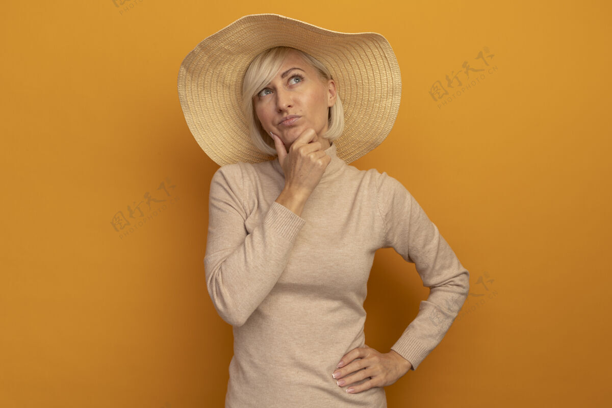 下巴体贴漂亮的金发斯拉夫女人 戴着沙滩帽 托着下巴看着橙色的一边姿势漂亮海滩
