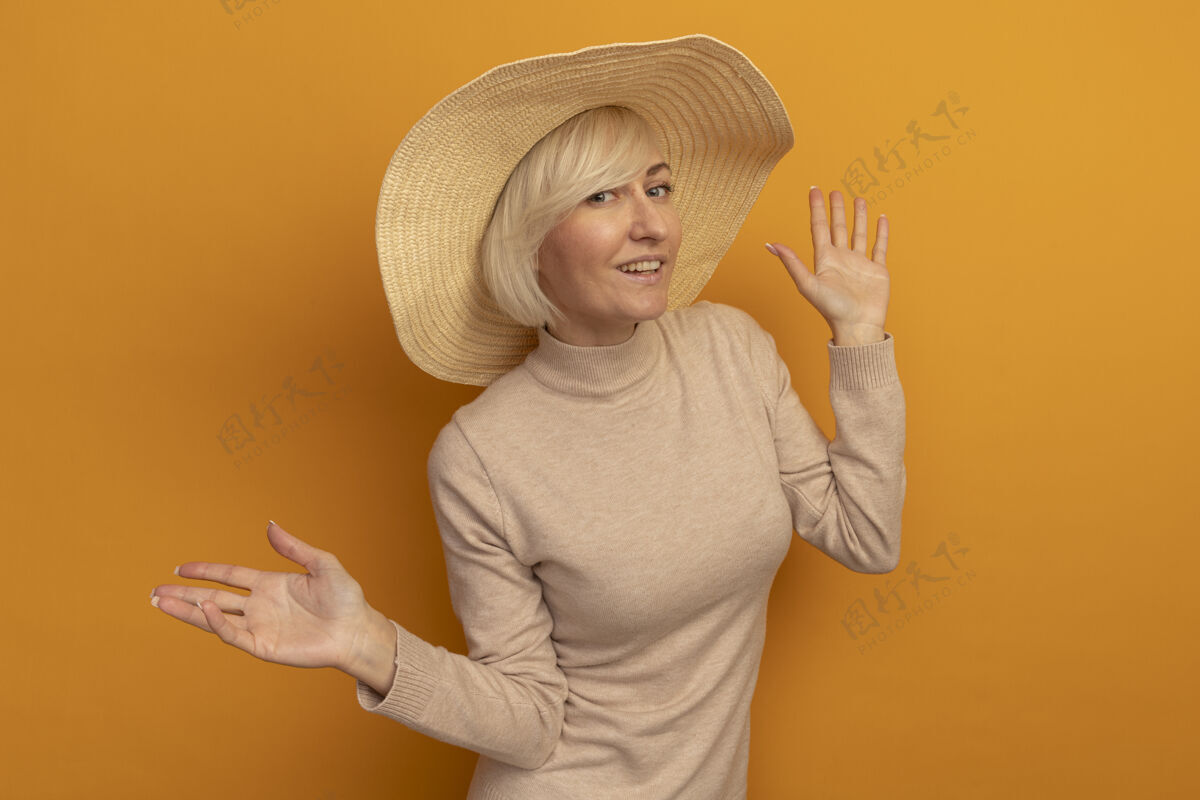 海滩微笑着的金发斯拉夫女人 戴着沙滩帽 举手站在橙色的沙滩上成人金发女人