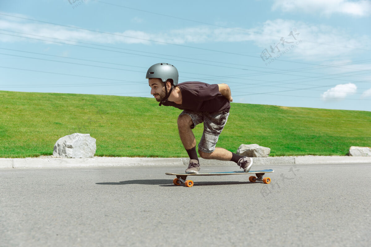 街道在阳光明媚的日子里 在城市街道上玩滑板的人年轻人在草地附近骑马 玩长板休闲活动 运动 极限 爱好和运动的概念城市乐趣男性