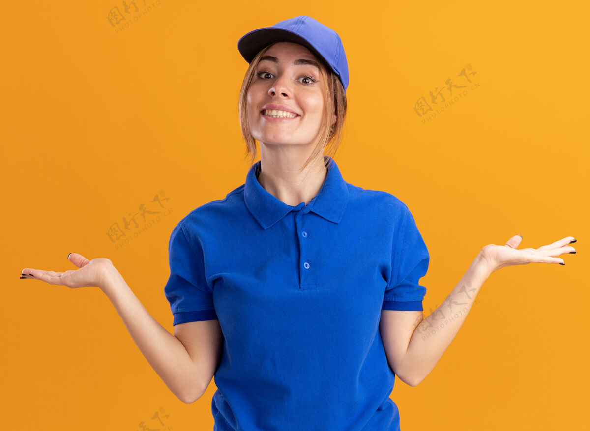 漂亮微笑着的年轻漂亮的女送货员穿着制服 手张开放在橘子上年轻姿势手