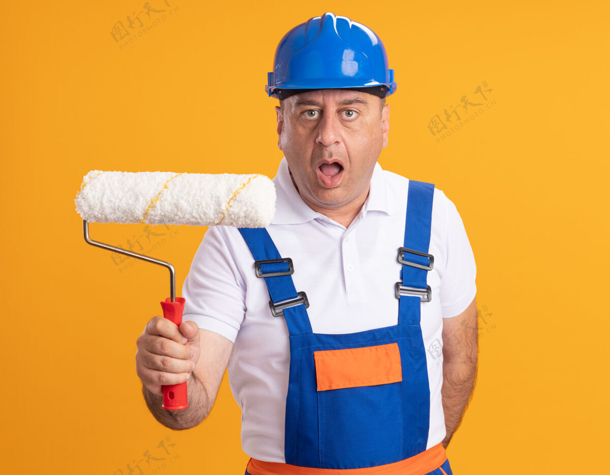 滚轴震惊的白人成年建筑工人在制服举行辊刷橙色建筑工人刷子男人