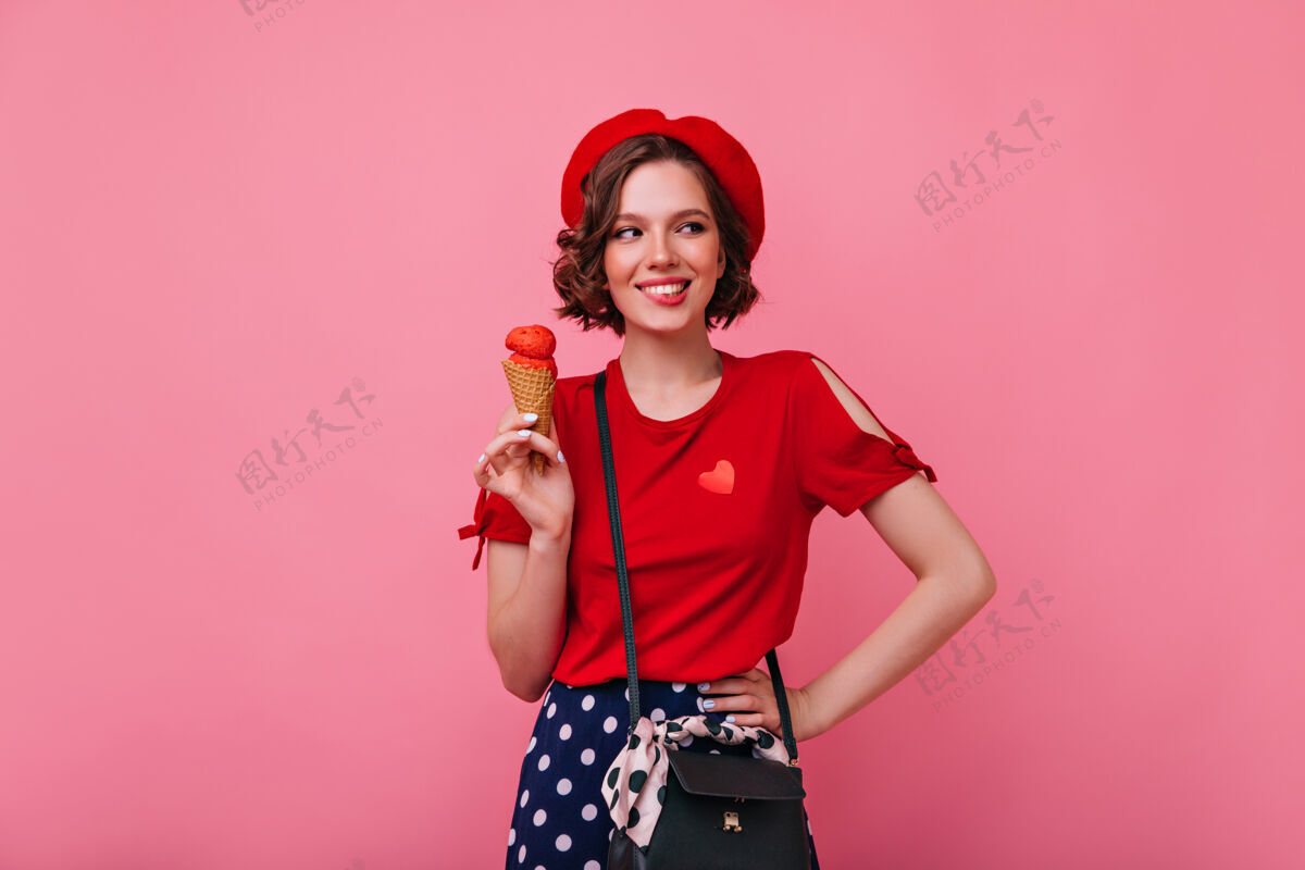 粉色热情的年轻女子穿着时髦的衣服吃冰淇淋室内照片微笑无忧无虑的女士与甜点时尚卷发女性