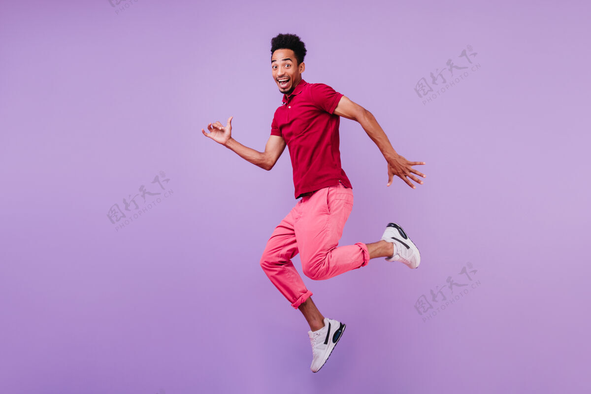 明亮积极无忧无虑的非洲男人穿着运动鞋跳舞帅气的高兴的家伙穿着粉色裤子笑着跳起来表情舞蹈模特