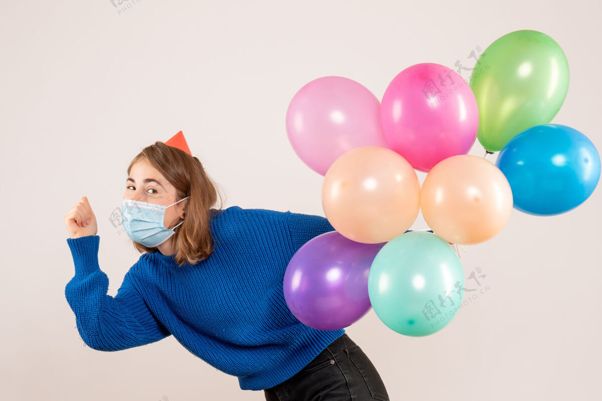 生日正面图：戴着消毒面具的年轻女性手持五颜六色的气球举行圣诞节乐趣