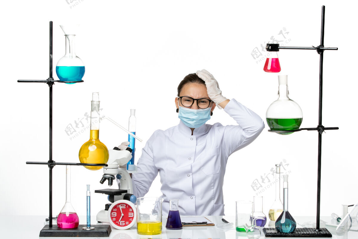 病毒前视图：穿着医疗服的女化学家 戴着面罩 拿着一个装有蓝色溶液的烧瓶 背景是白色的病毒化学实验室的covidsplash医生医学实验室