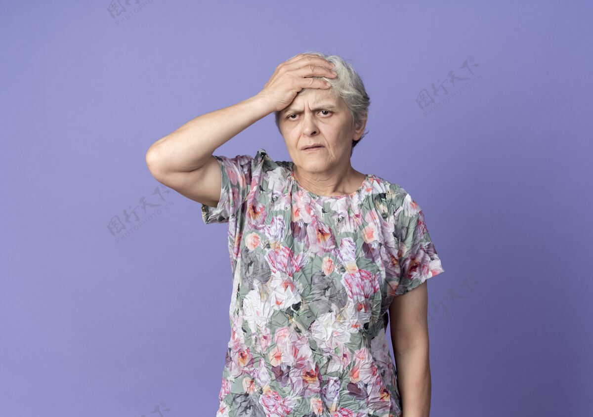 前额不高兴的老妇人把手放在前额上 孤零零地看着紫色的墙上手老不高兴