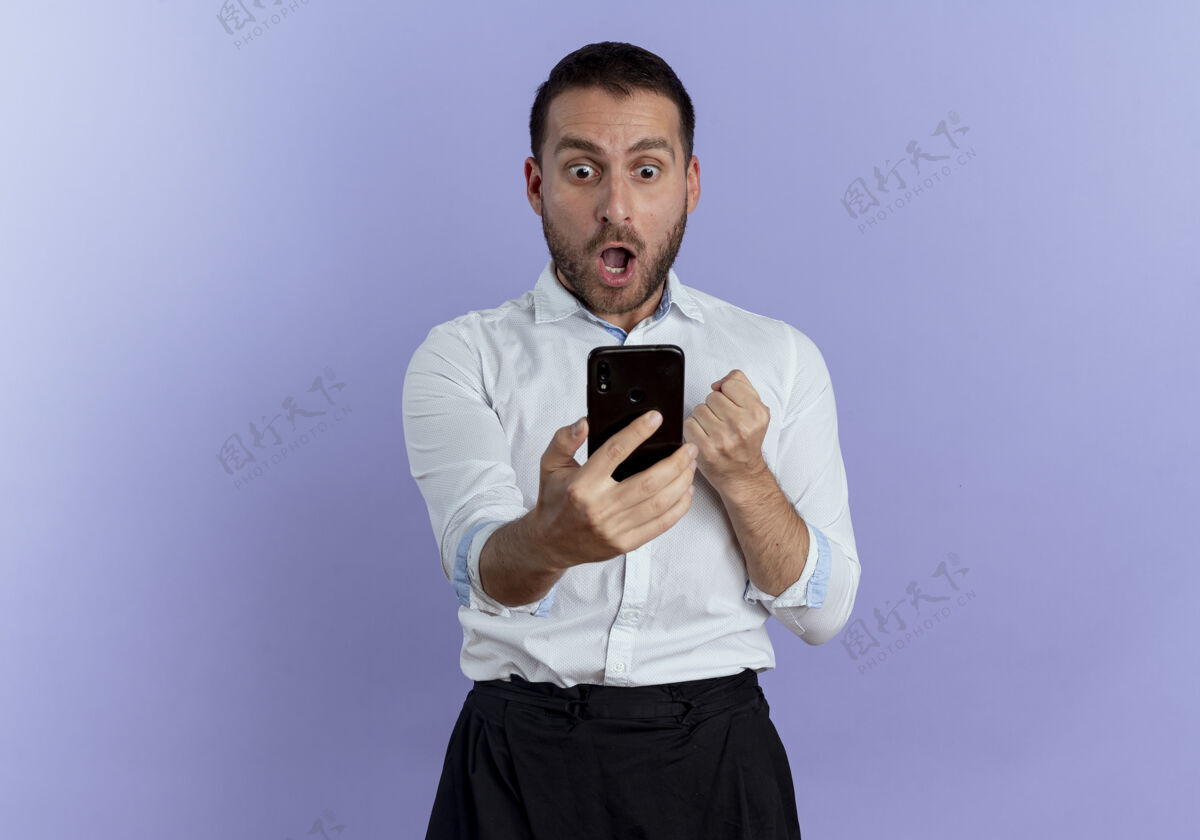 兴奋兴奋的帅哥拿着手机看着隔离在紫色墙上的手机电话拿着男人