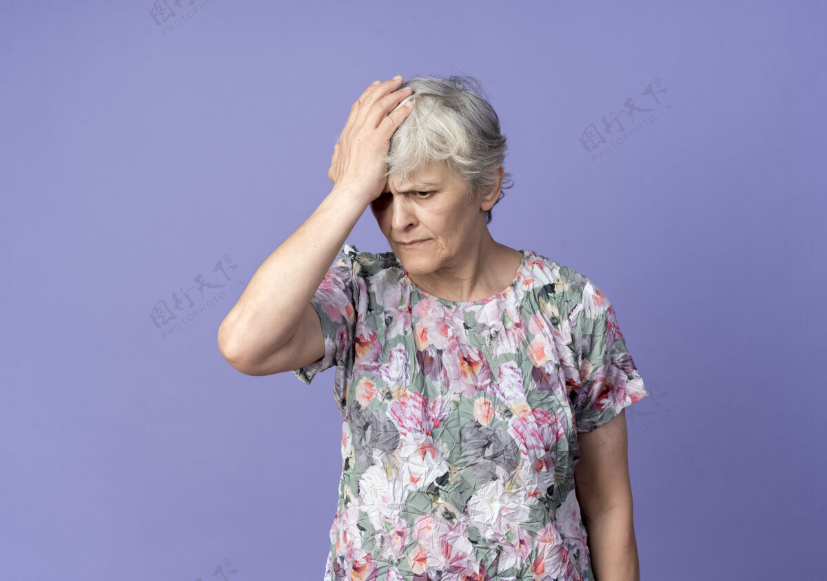 额头不高兴的老妇人把手放在隔离在紫色墙上的前额上不高兴老老