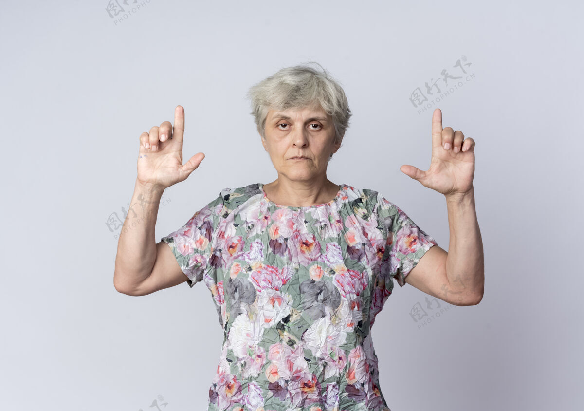 点自信的老妇人用两只手孤立地指着白墙上向上信心女人
