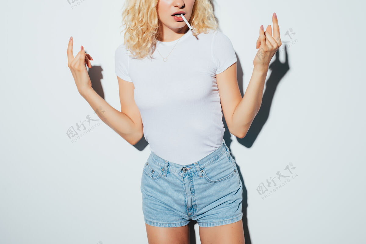 女性特写镜头：身穿白色t恤的金发女子 身上有摇滚标志 从隔离在白色墙上的雪茄中喷出烟雾漂亮时髦问题