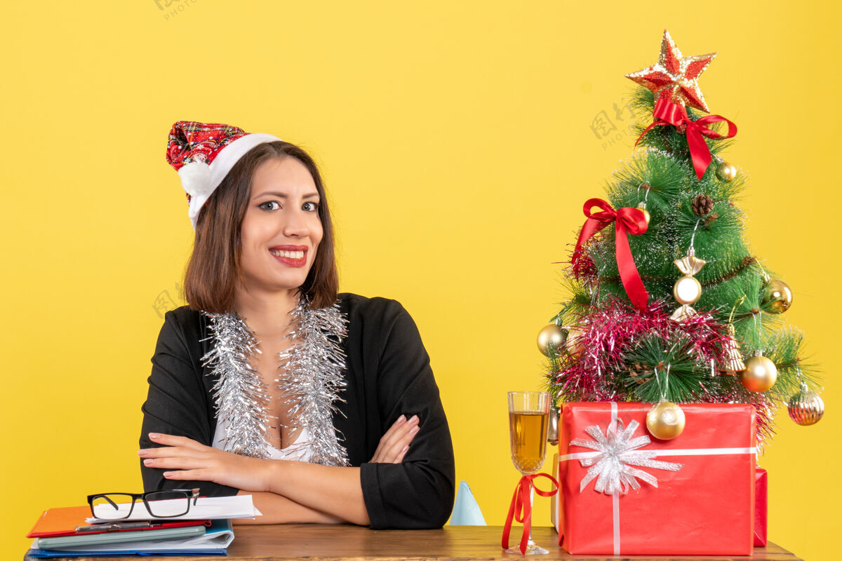 树穿着西装 戴着圣诞老人帽 戴着新年装饰品 手里拿着文件 坐在一张桌子旁 桌子上放着圣诞树漂亮西装快乐