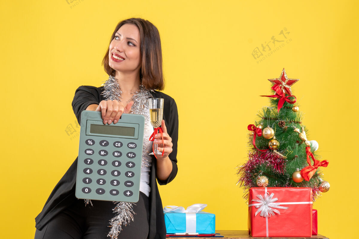 性感圣诞心情与满意美丽的女士站在办公室里 拿着计算器在黄色的办公室里举酒酒成人头发