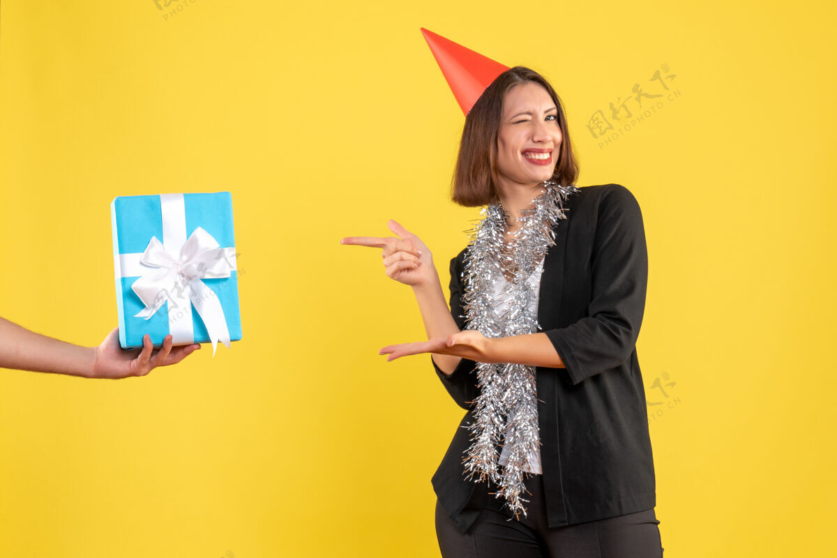 人圣诞心情与快乐和兴奋的商务女士在西服与xsmas帽子指向手拿着礼物在黄色心情成人圣诞节