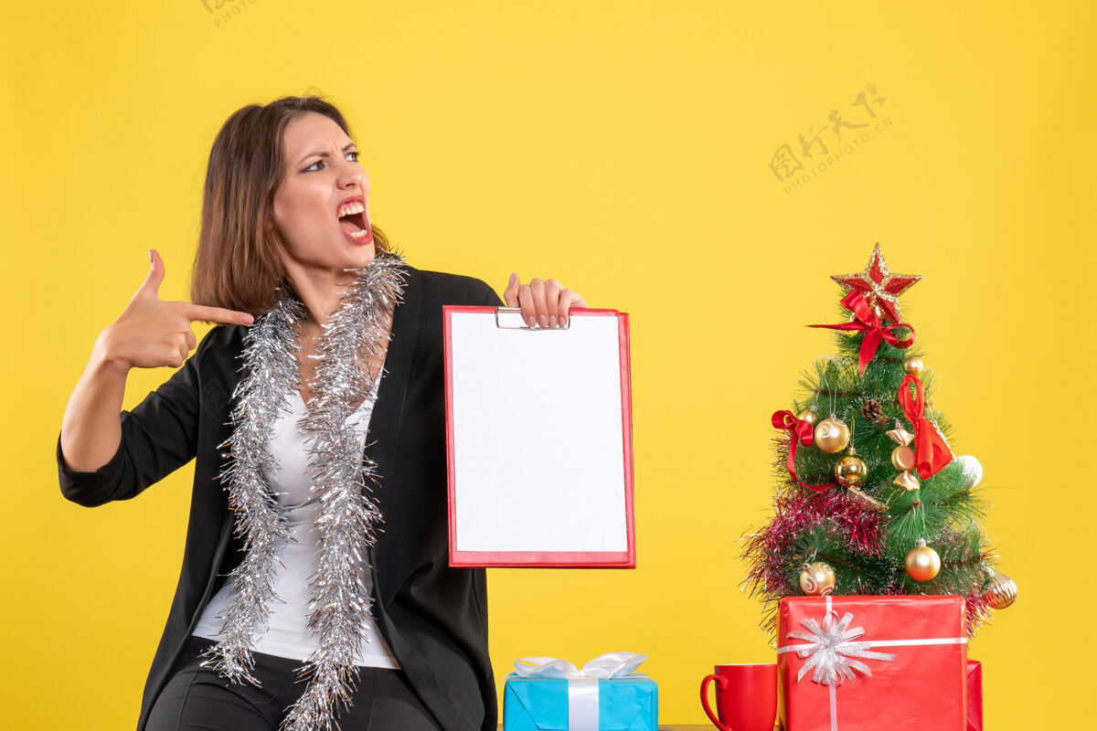 黄色圣诞节的心情与情感美丽的女士站在办公室和指向文件在办公室的黄色衣服指向心情
