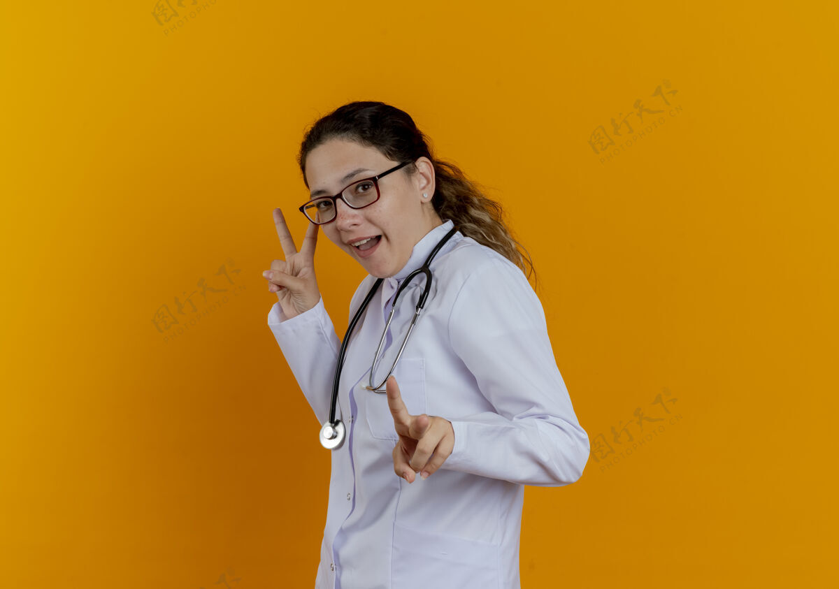 穿快乐的年轻女医生穿着医用长袍 戴着眼镜听诊器 表情平静听诊器人和平