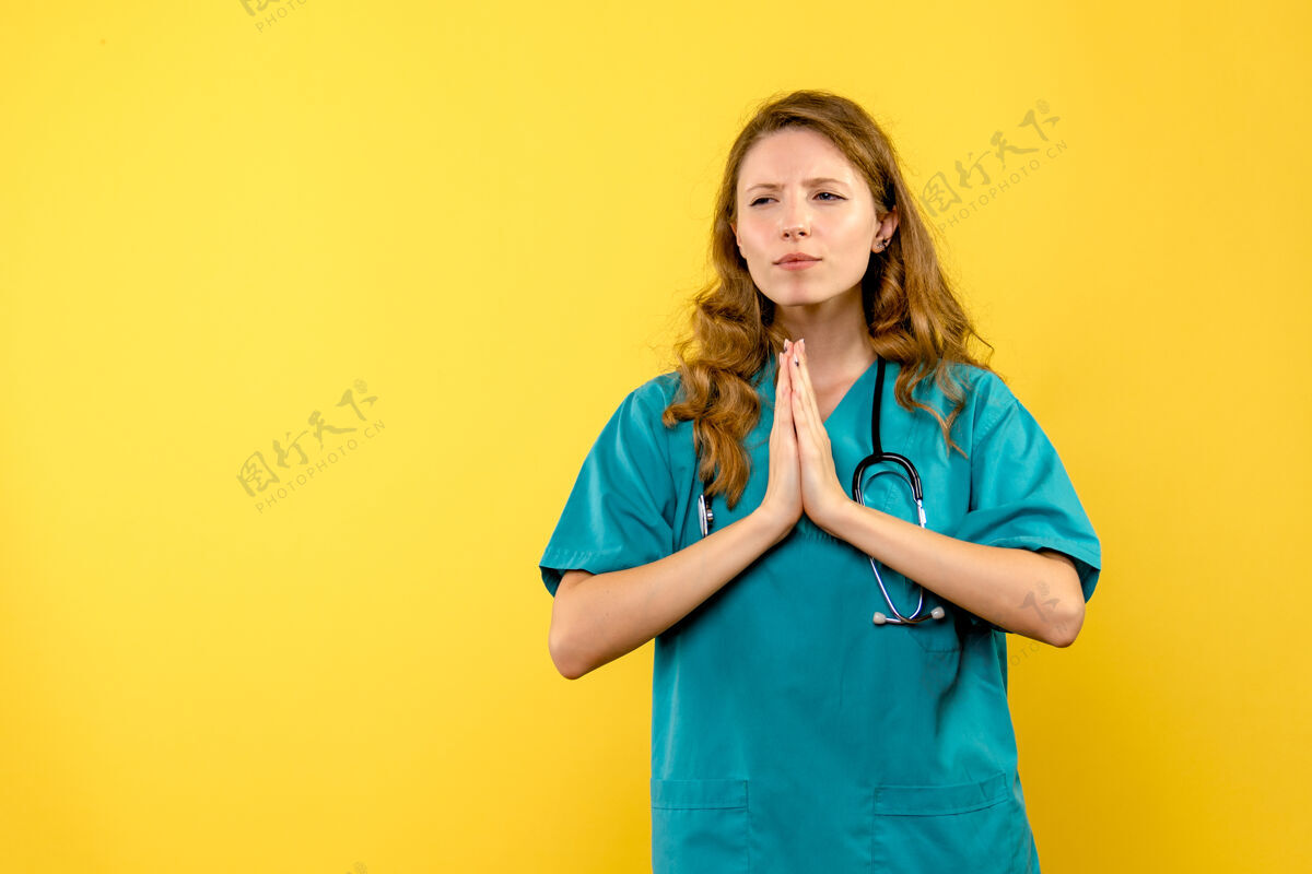 女人黄色墙壁上女医生祈祷姿势的正视图女士漂亮前面