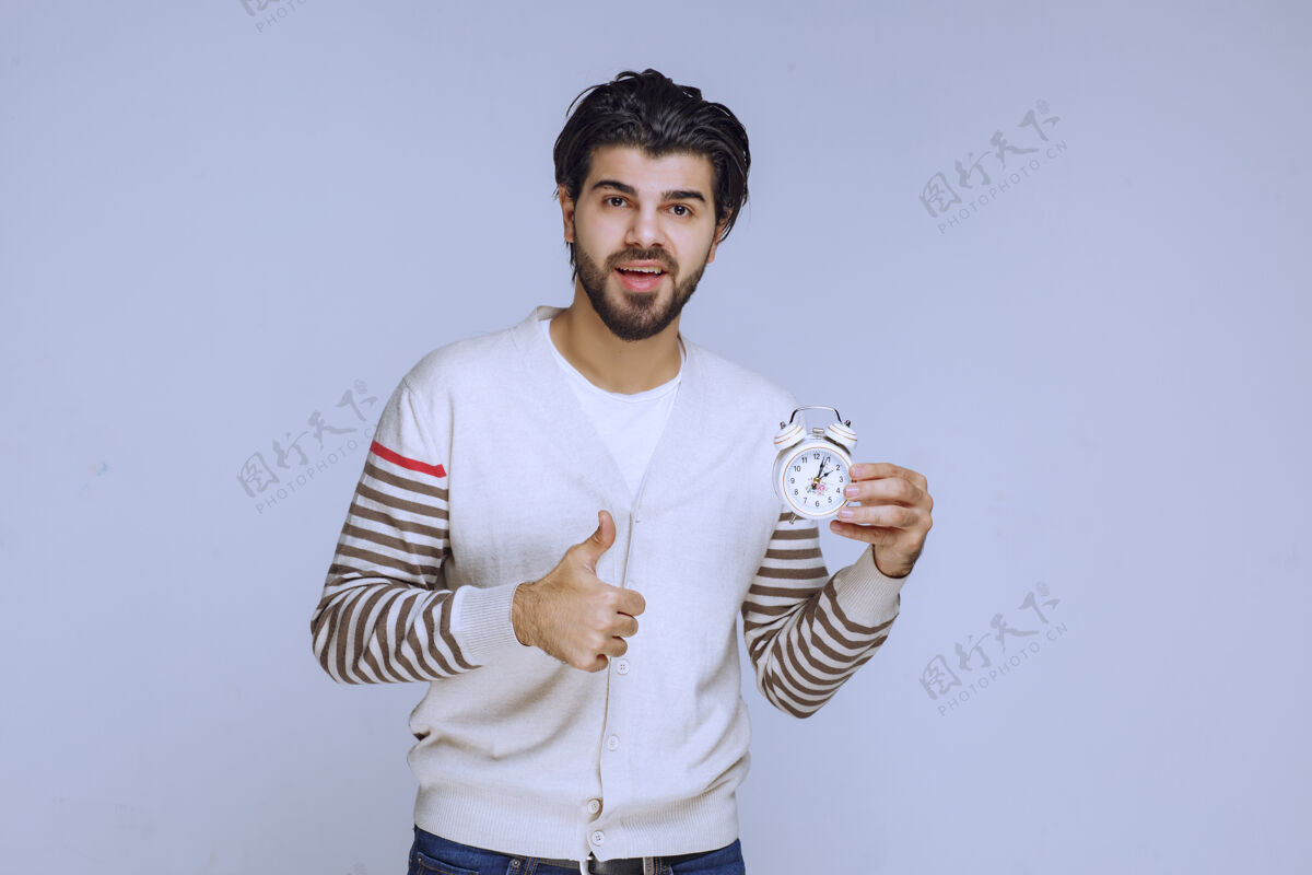 休闲一个拿着闹钟的男人 展示着它的工作原理和享受产品模特年轻人
