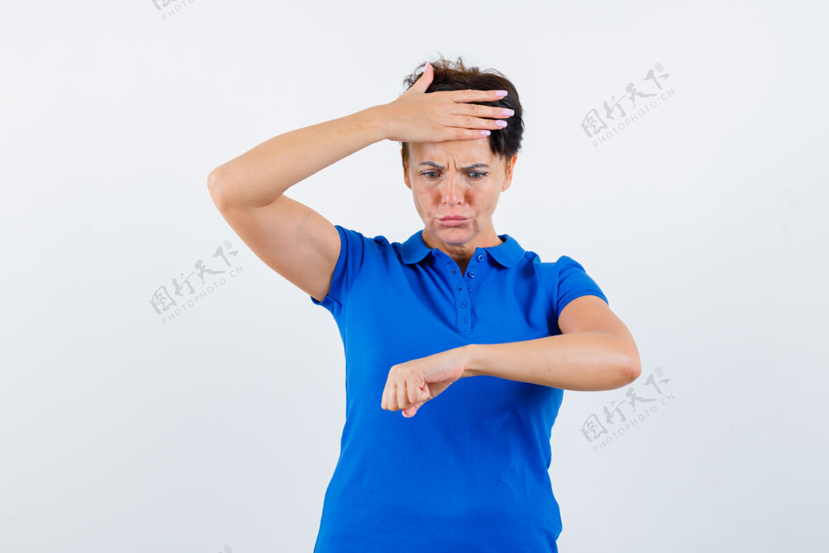 休闲一幅成熟女人的画像 她穿着蓝色t恤 假装看着手腕上的手表 惊恐地看着前方前面健康美容