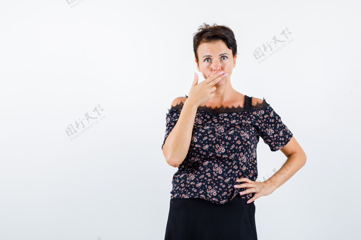 人成熟的女人一只手放在腰上 一只手捂着嘴 穿着花衬衫和黑色裙子 看起来很严肃 正面照肖像花卉嘴