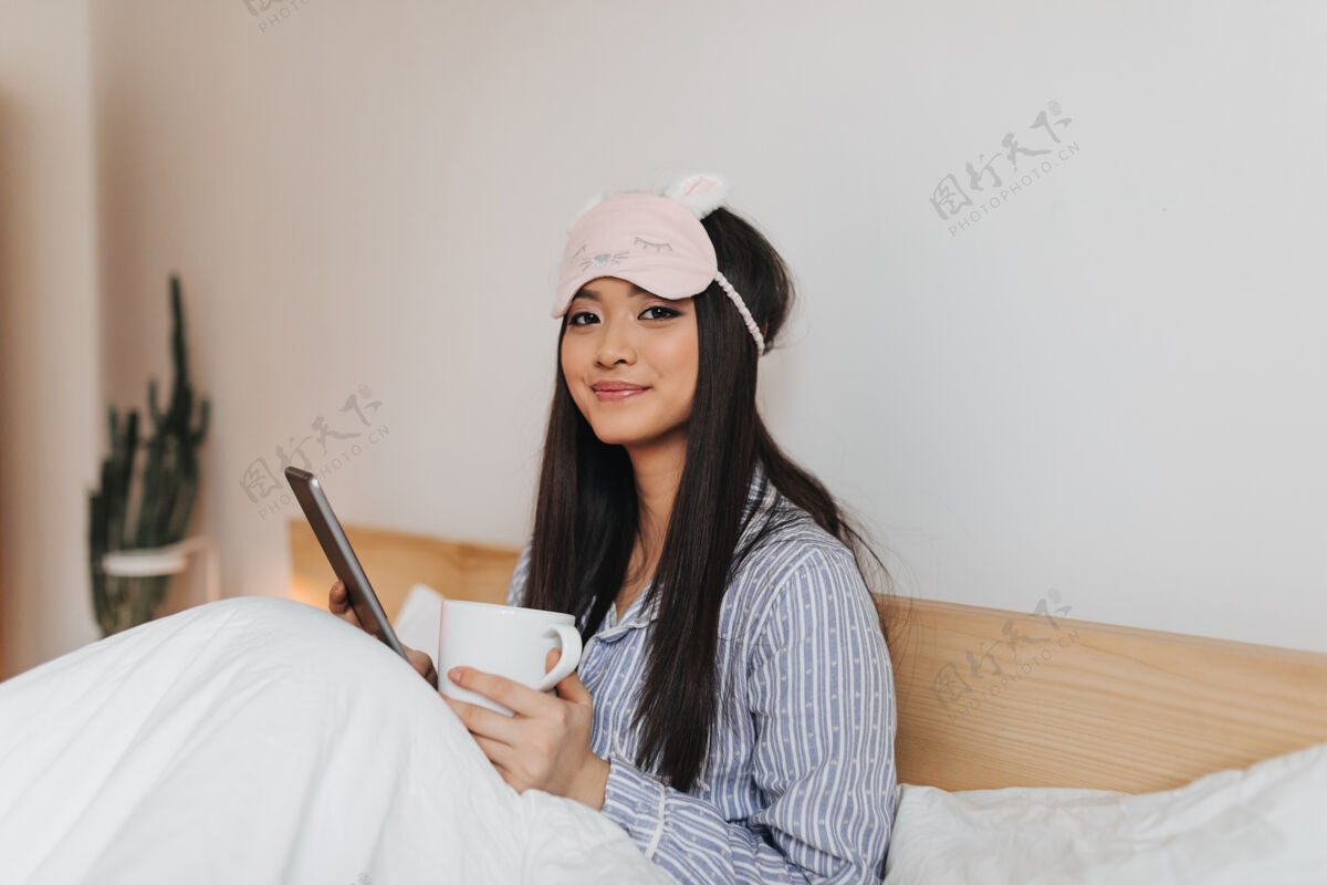 女人长着一头光滑长发的漂亮女人躺在床上端着一杯茶房子早晨床上用品