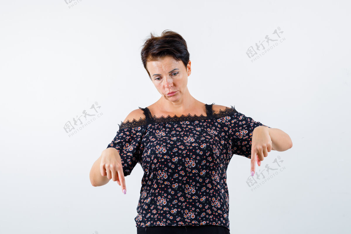 健康成熟的女人穿着花衬衫 黑色裙子 用食指指着下面 看起来很严肃正面图衬衫正面年龄