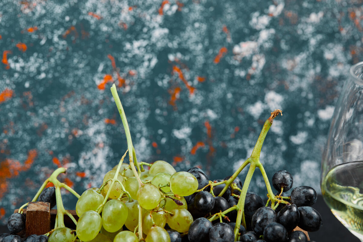 葡萄白色和黑色的葡萄与一杯葡萄酒在蓝色的背景高品质的照片葡萄酒水果串