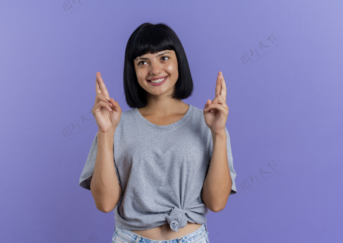 黑发微笑的年轻黑发白种女孩交叉手指看着紫色背景上孤立的一面和复制空间壁板微笑空间