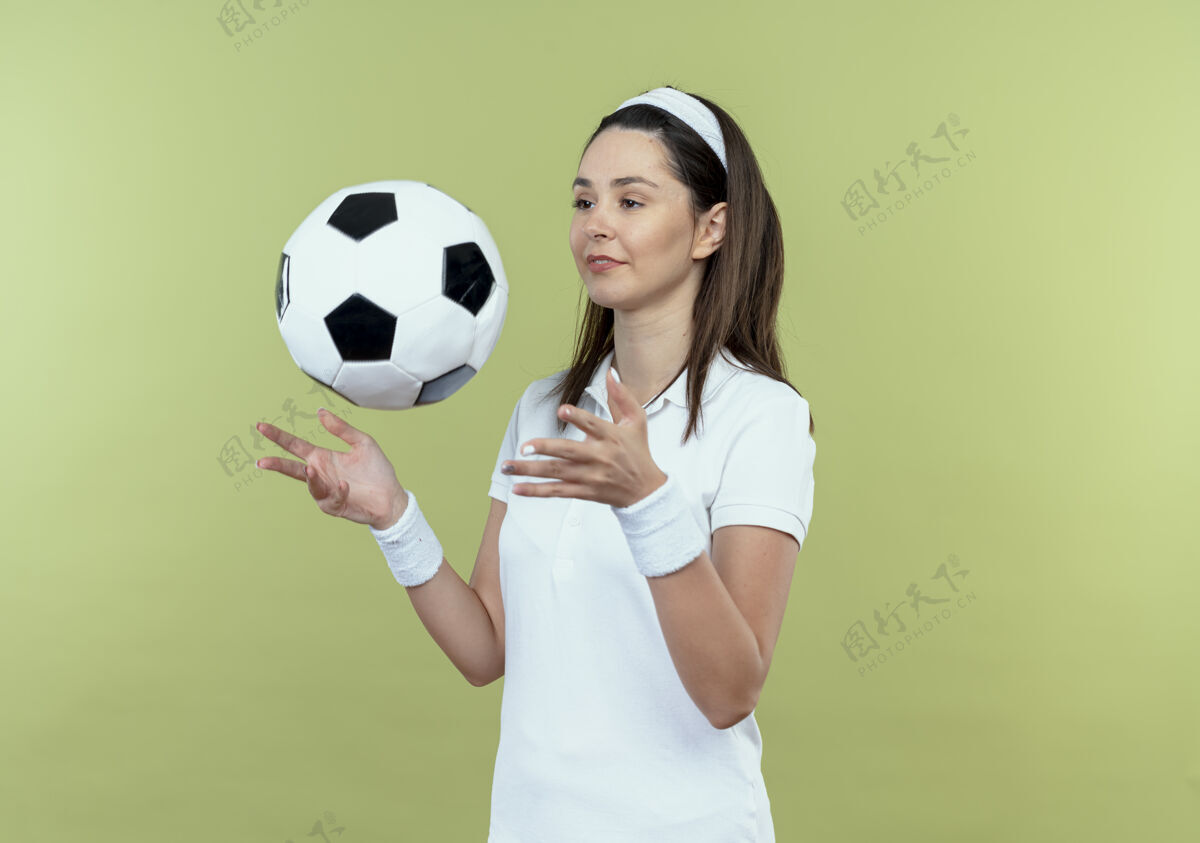 投掷戴着头巾的年轻健身女士在灯光背景下自信地微笑着扔足球健身站立足球