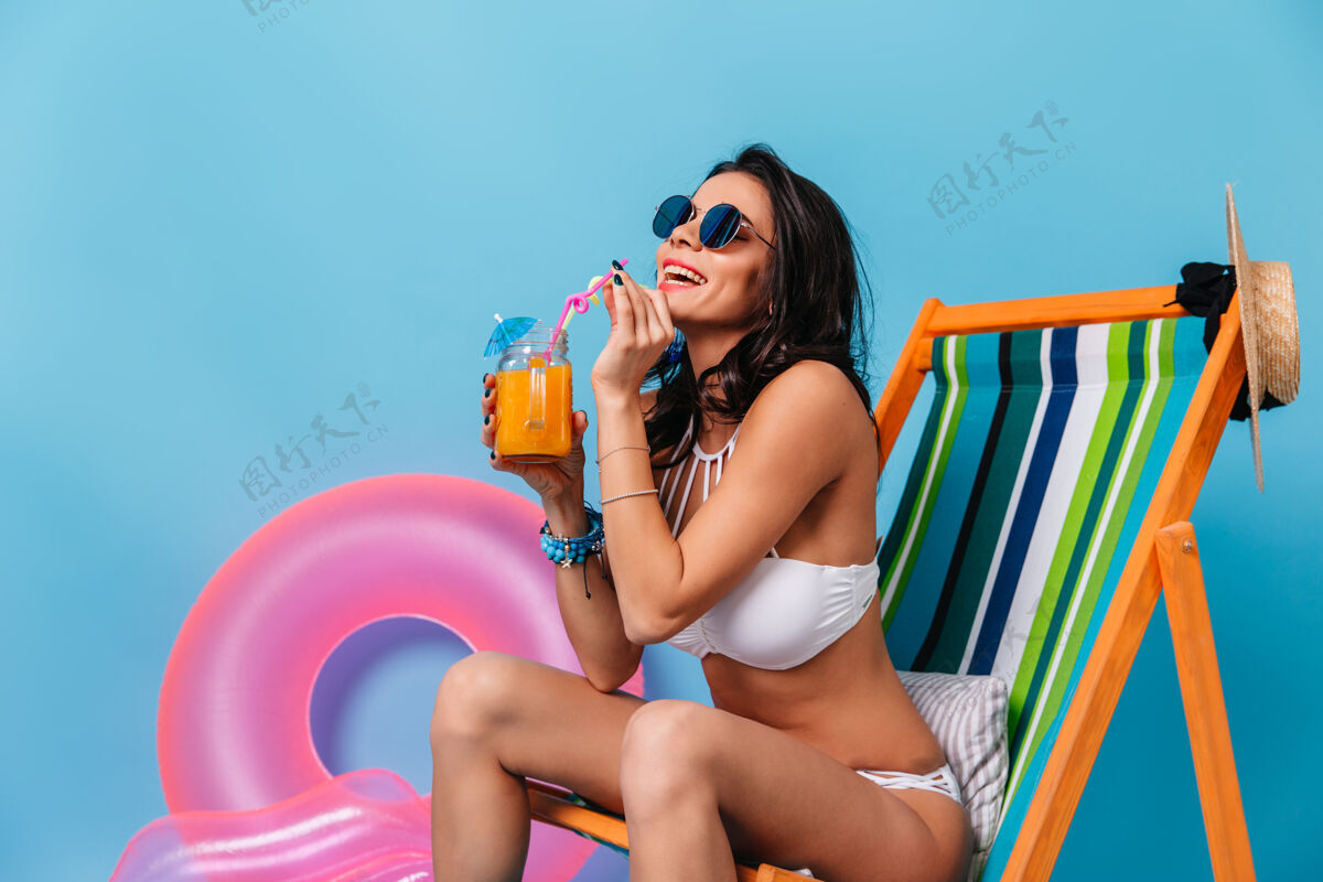 女孩迷人的棕褐色女人坐在躺椅上喝鸡尾酒微笑人年轻人