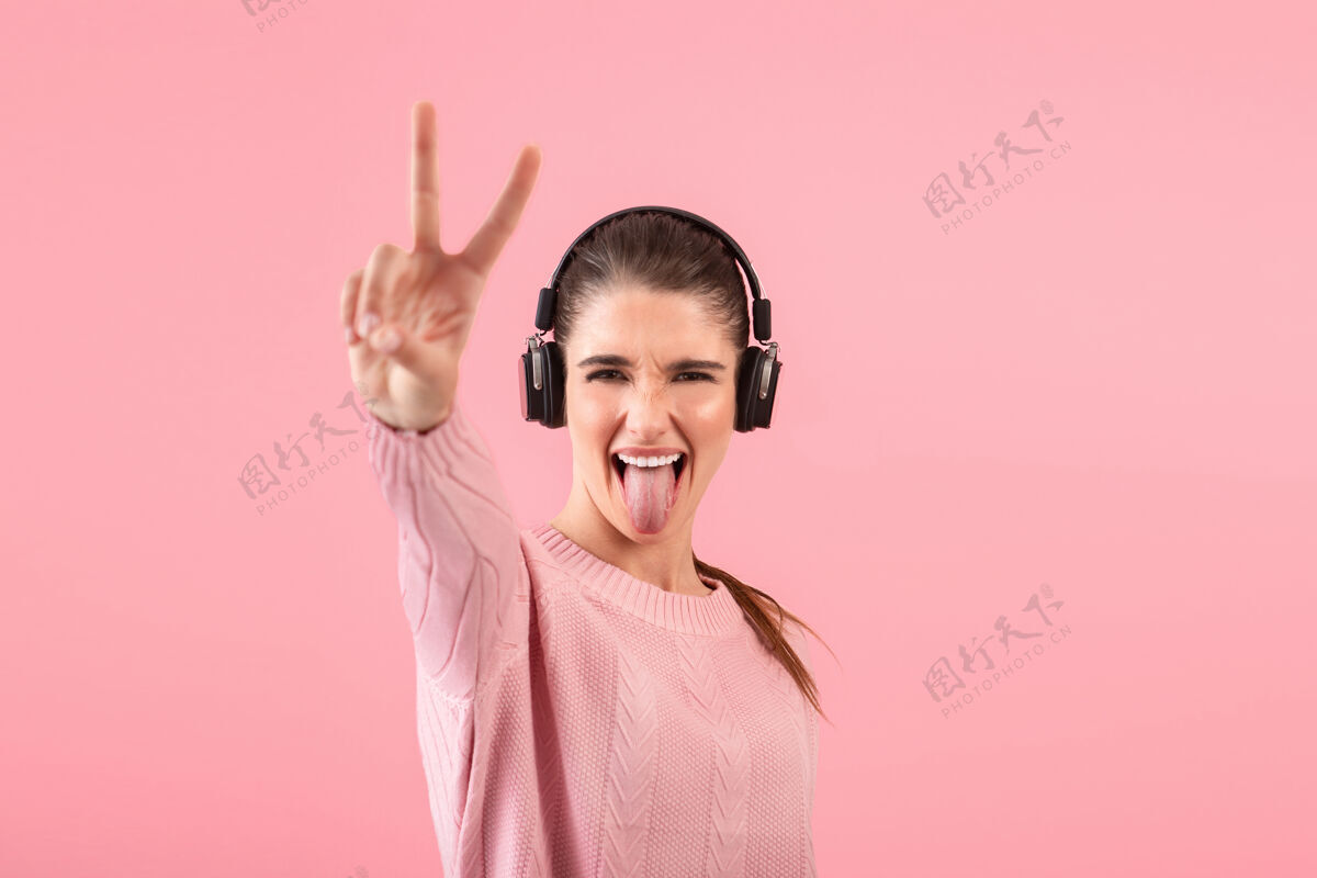 欢呼年轻漂亮的女人戴着无线耳机听音乐 穿着粉色毛衣微笑着设备声音年轻人
