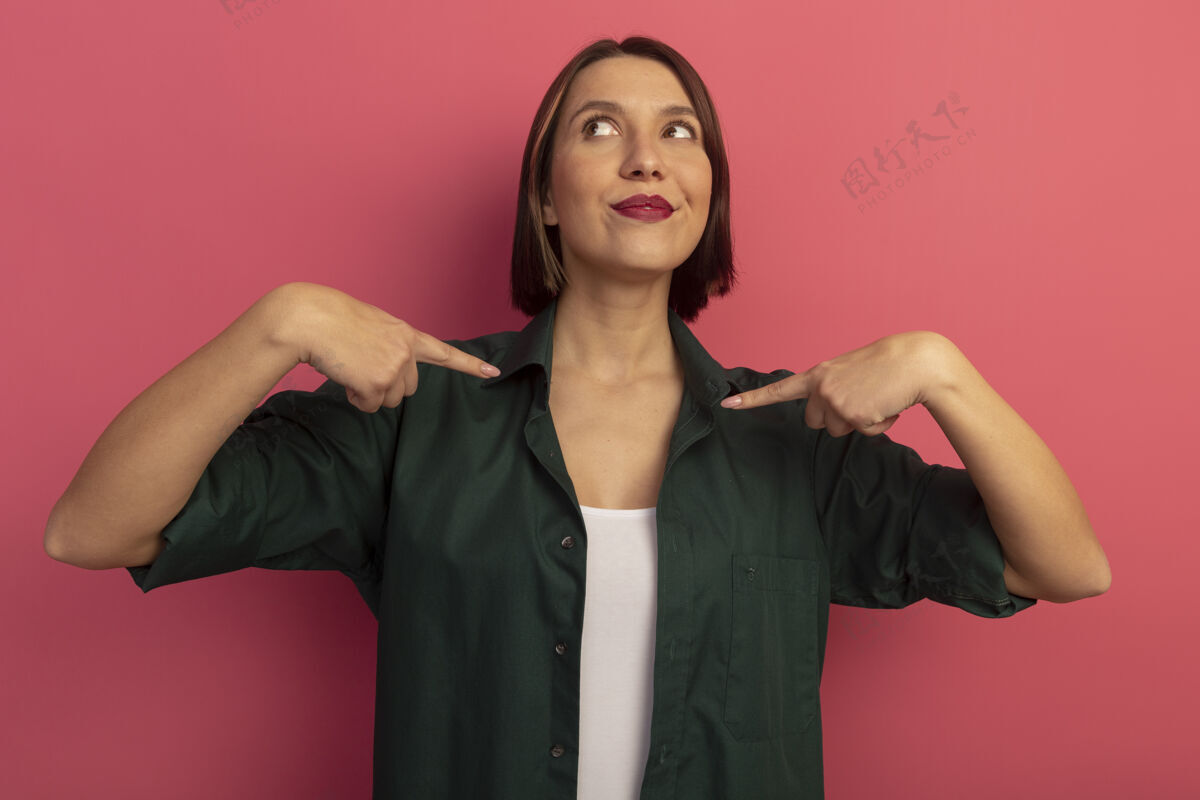 手可爱的女人指着自己 两手分别放在粉红色的墙上人衣服女人