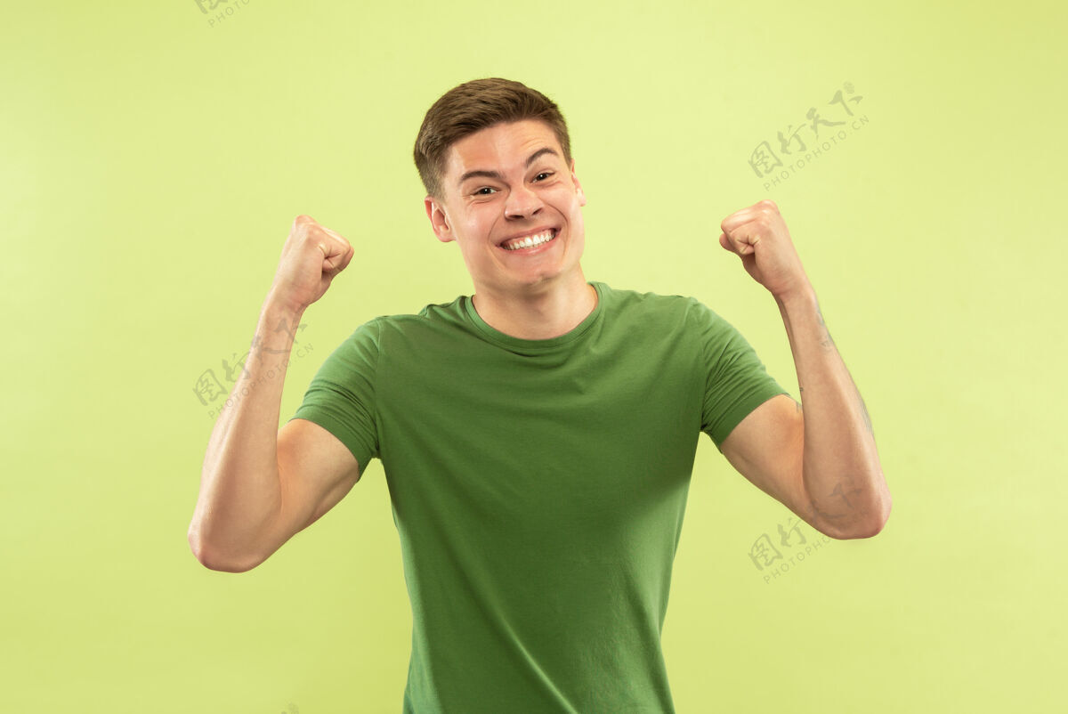 财务绿色工作室背景上的白人青年半身肖像穿着衬衫的漂亮男模人类情感的概念 面部表情 销售 广告疯狂的快乐 庆祝 震惊人面部肖像