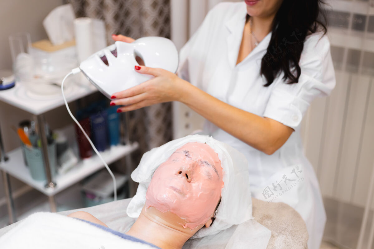 美容师客户躺在美容桌上的沙龙里 脸上戴着白色的面具面部皮肤科女性