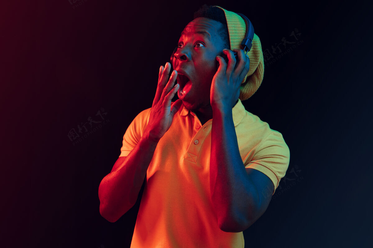 人物年轻帅气的快乐惊喜的时髦男人在霓虹灯下用耳机听音乐迪斯科舞厅 夜总会 嘻哈风格 积极的情绪 面部表情 舞蹈概念帅哥帽子非洲