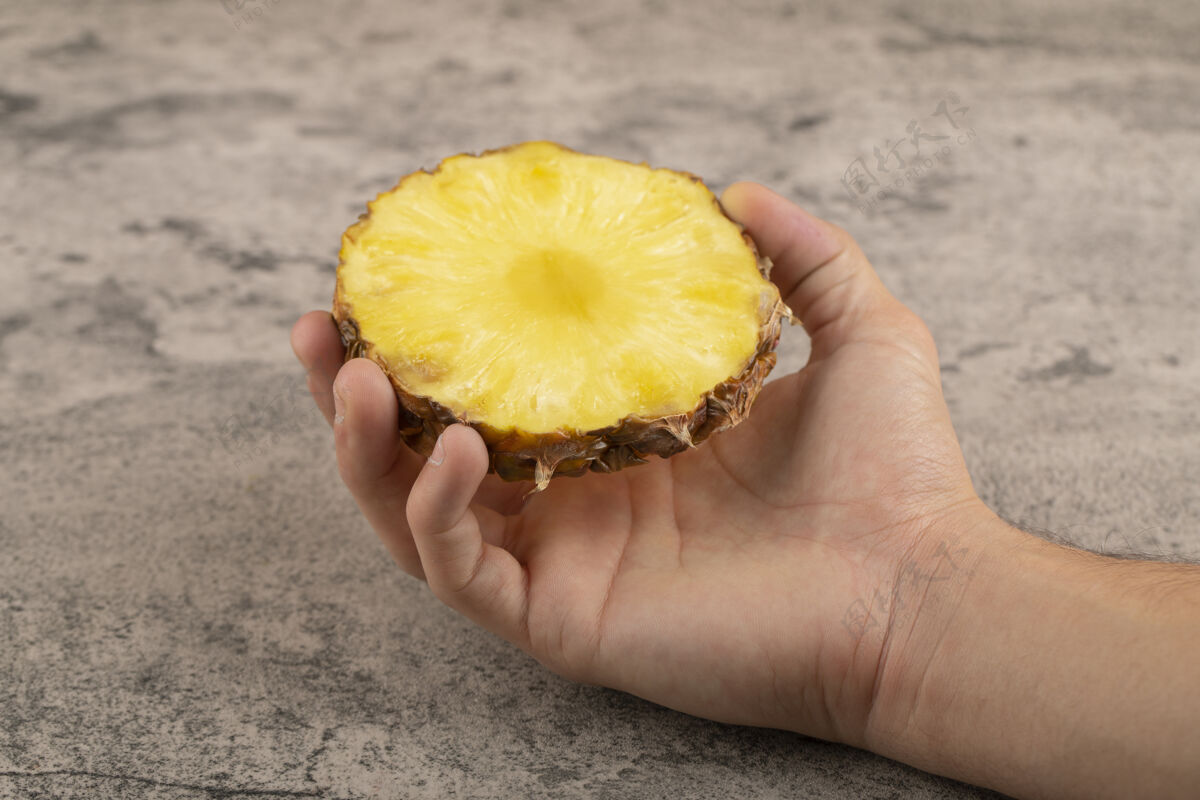 生的男人的手拿着半个菠萝放在石头上热带Ananas异国情调
