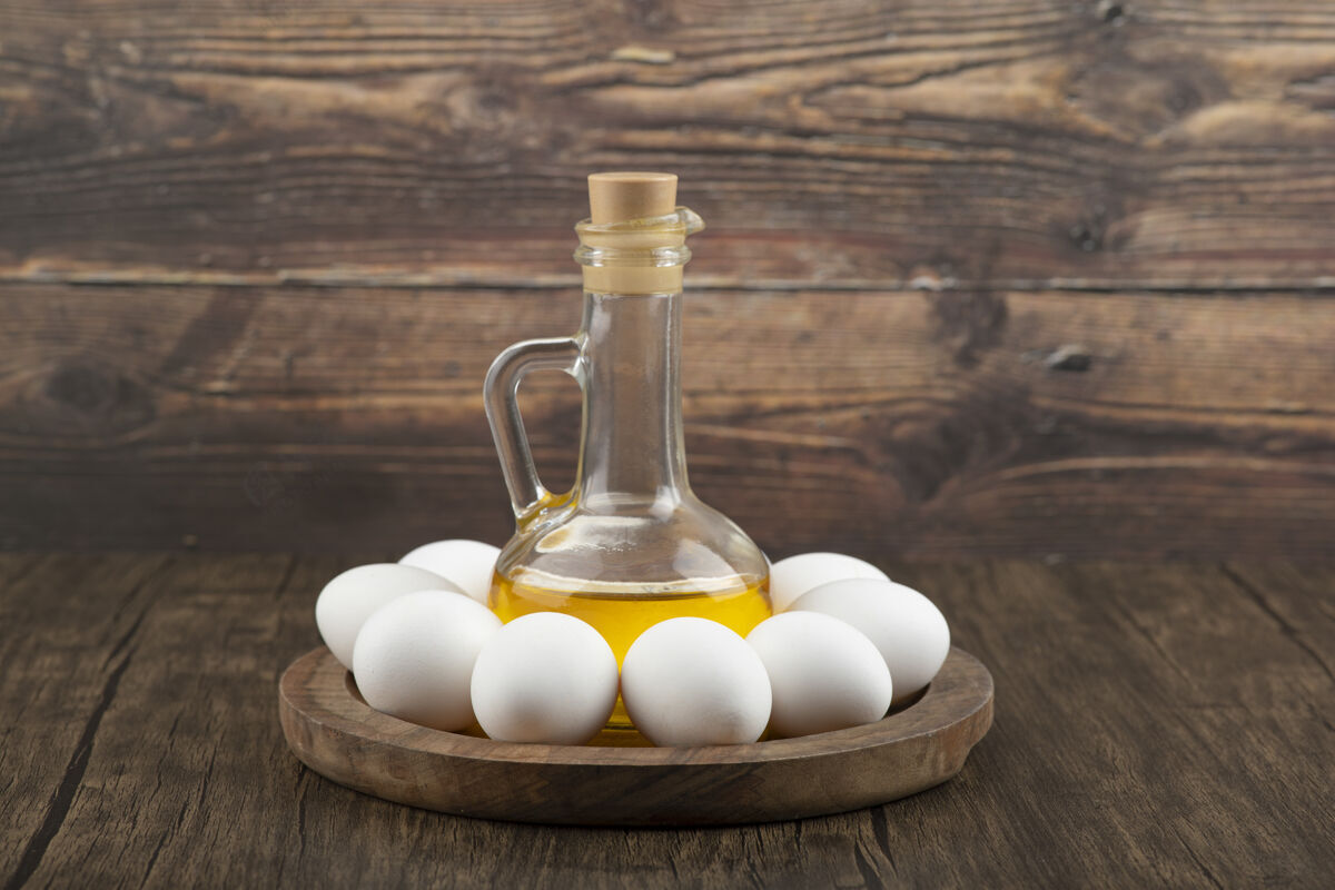 有机生白鸡蛋和一瓶橄榄油放在木板上烹饪油生的