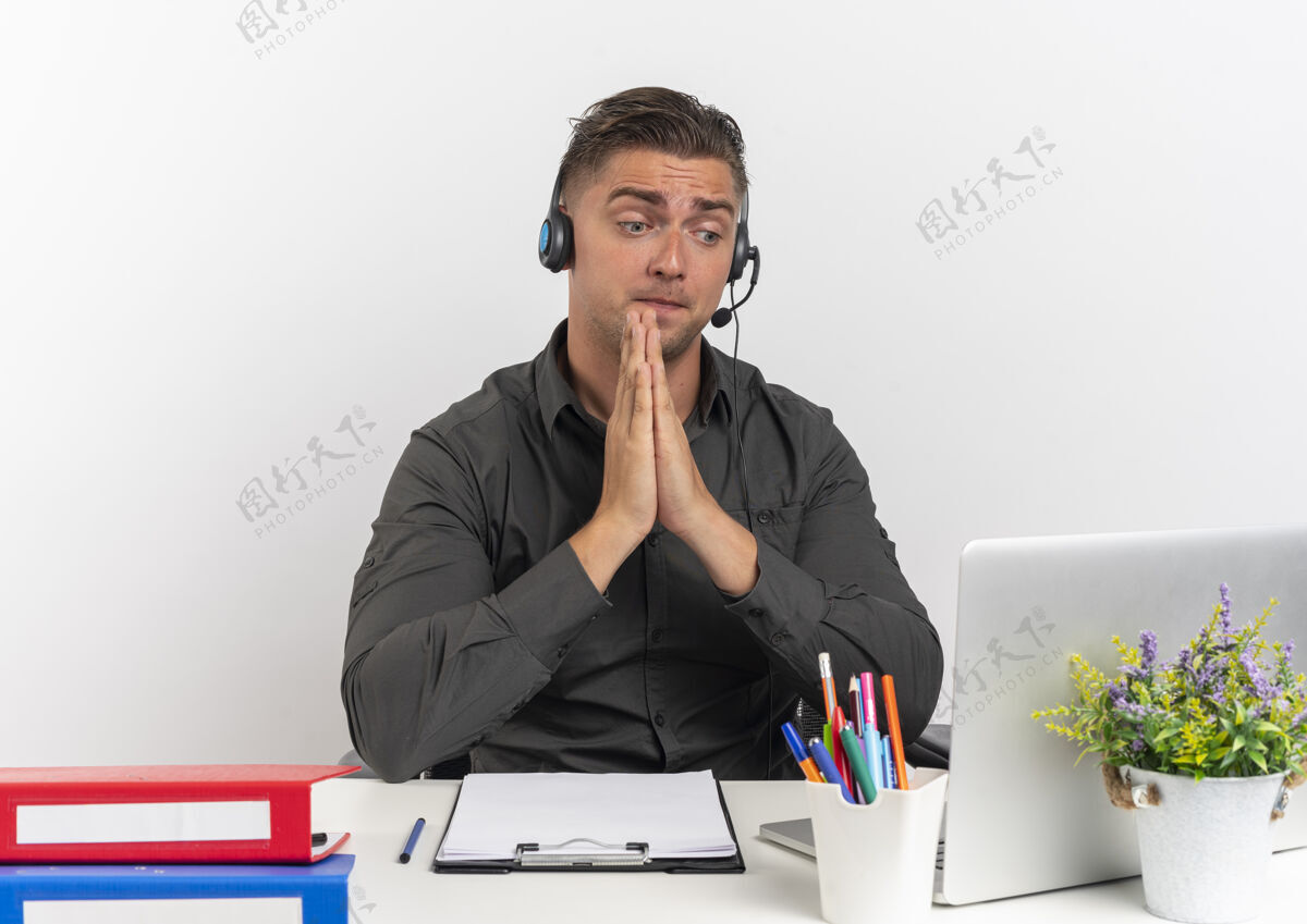工作人员年轻惊讶的金发上班族戴着耳机坐在办公桌前拿着办公工具看着笔记本电脑手拉着手在白色背景上与复印空间隔离金发笔记本电脑拿着