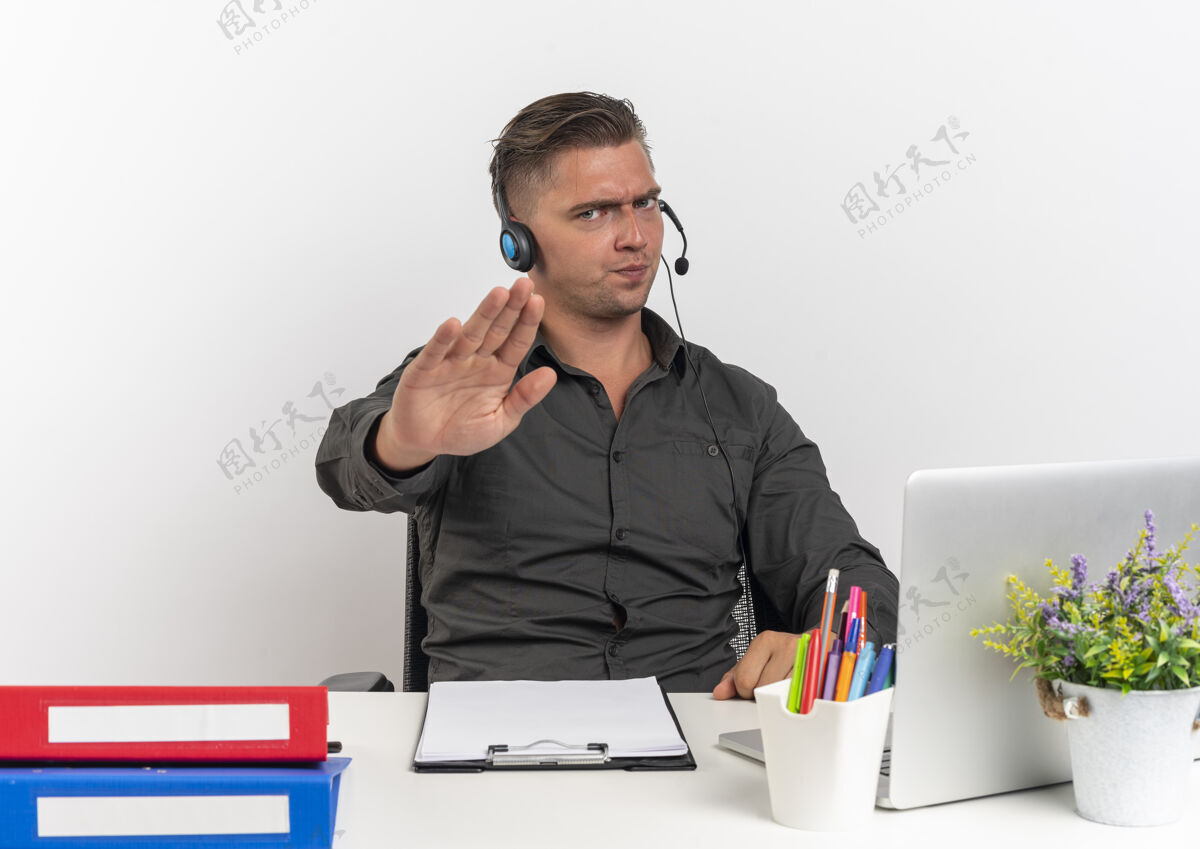 耳机年轻恼怒的金发上班族戴着耳机坐在办公桌旁 拿着办公工具 用笔记本电脑做手势 停止手势 在白色背景上隔离 留有复印空间工人手办公室
