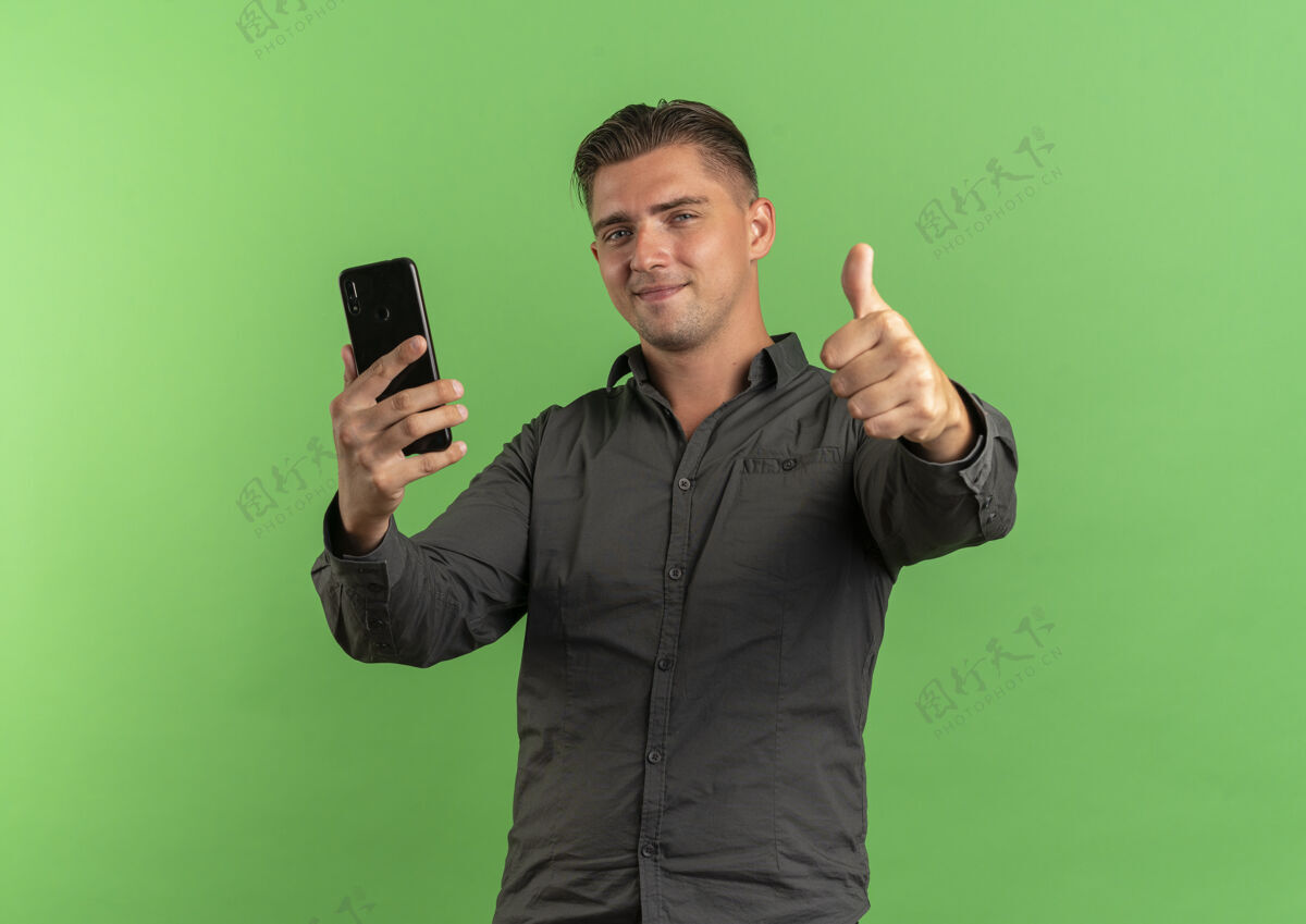 帅气年轻快乐的金发帅哥拿着电话 竖起大拇指 在绿色的背景上与复印空间隔离金发电话年轻
