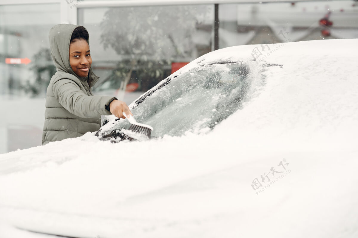 寒冷冬天非洲女人在车上扫雪的肖像穿着绿色夹克的女人女孩汽车冬天