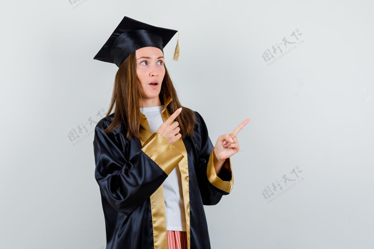 前面年轻的女毕业生穿着学院服指着右上角 疑惑地看着前方自然毕业健康