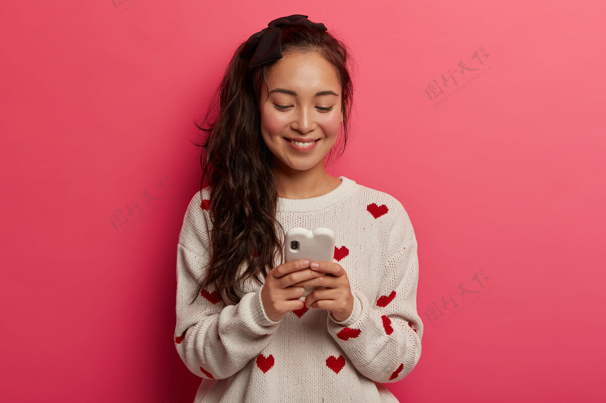 在线带着温柔微笑的少女 在现代手机上输入信息 在线聊天 在社交网络上阅读帖子 对科技上瘾博客套头衫手机