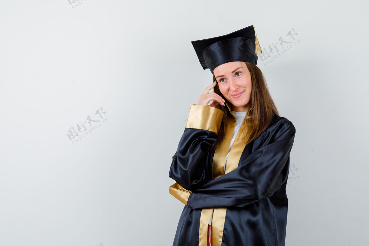 人民女毕业生身着学院服站在思考的姿势 欢快地看着前方思想长袍骄傲