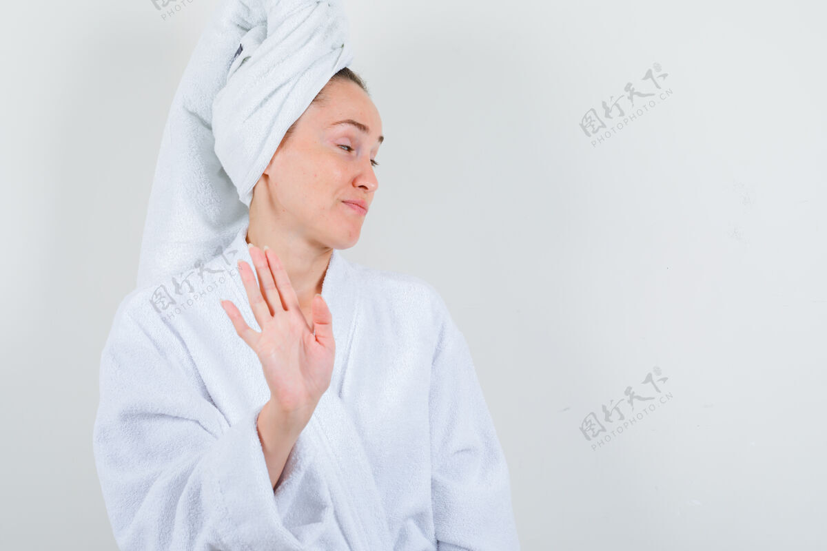 护理身穿白色浴袍的年轻女士 毛巾显示停止手势 看起来不满意 正面视图模特水疗女士