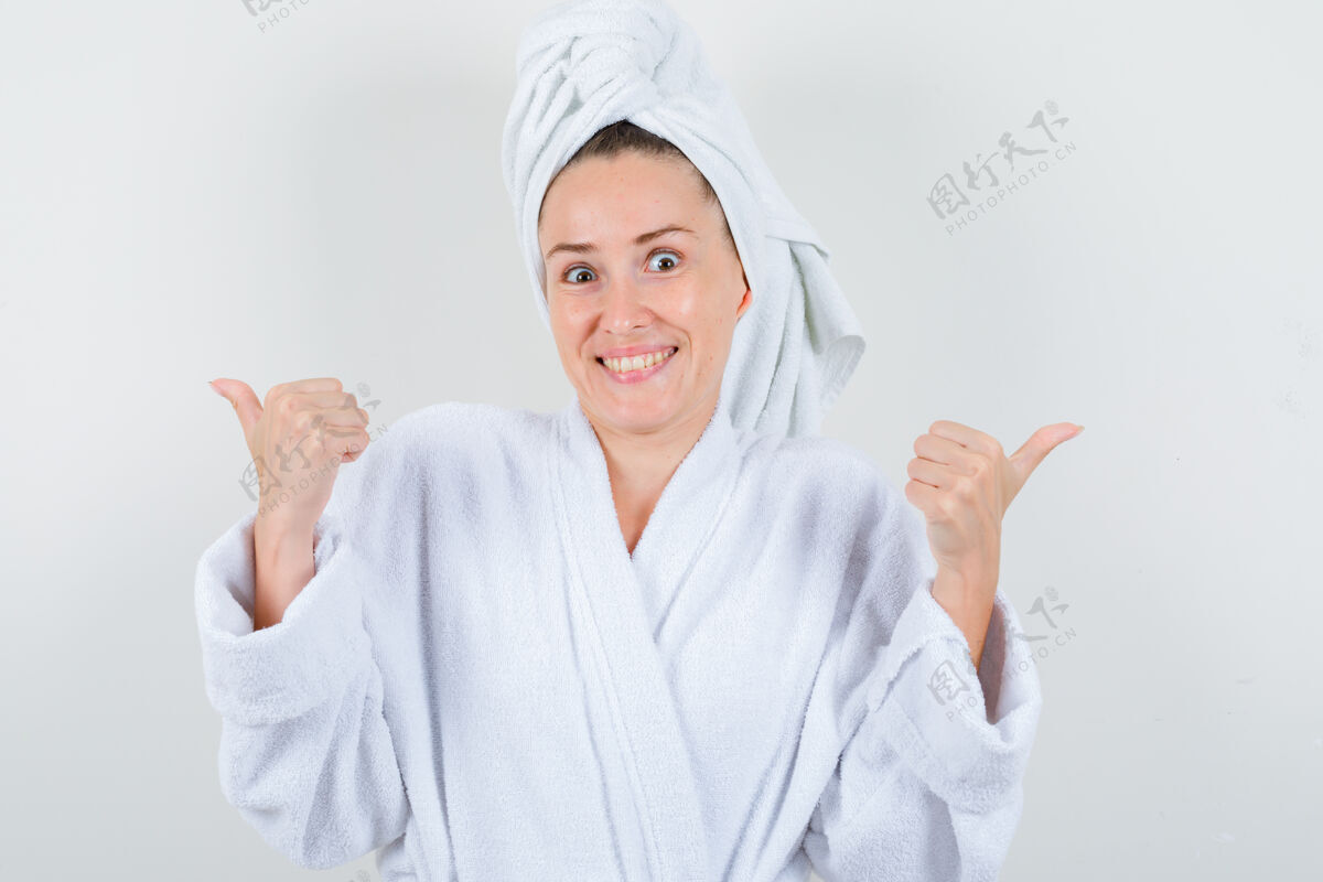健康身穿白色浴袍的年轻女子 毛巾上竖起大拇指 看上去很开心 正前方的景色肖像毛巾乐趣