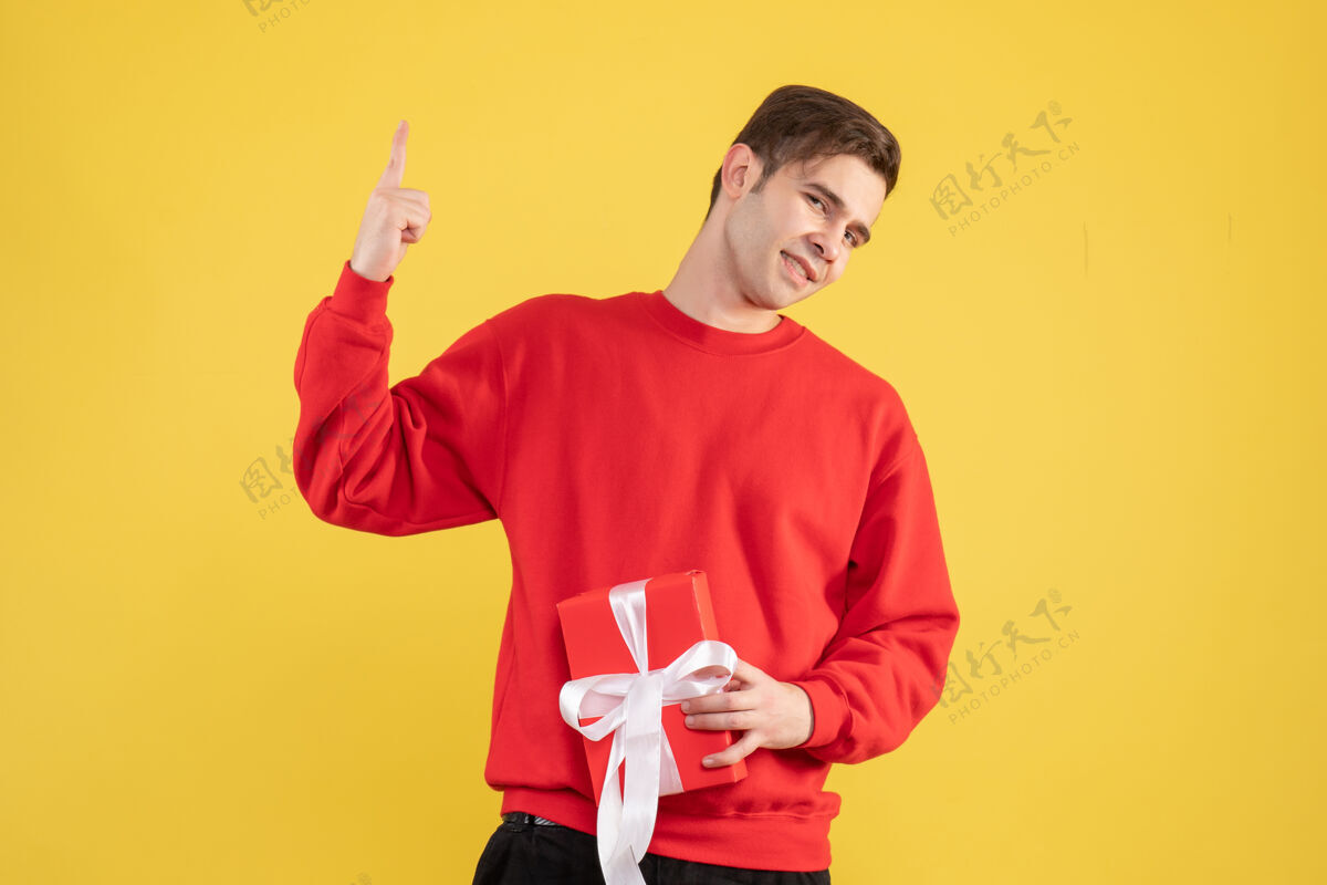 男人正面图：穿着红色毛衣的年轻人用手指指着黄色背景年轻人向上肖像