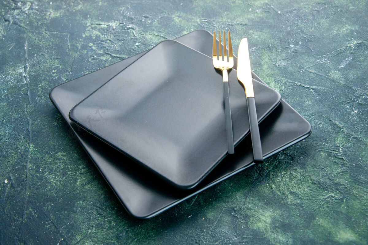 叉子前视图黑色方形板 深蓝色背景上有金色的刀叉刀晚餐厨房