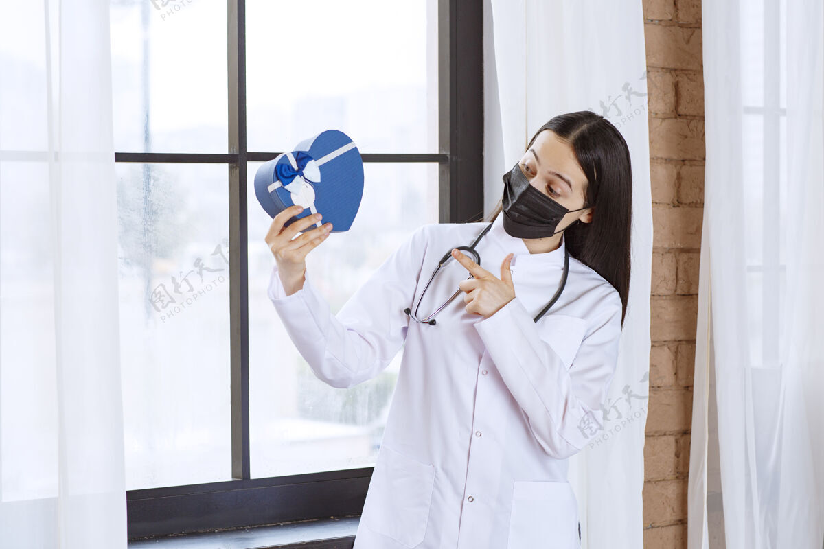 模特医生拿着听诊器和黑色口罩 手里拿着一个蓝色心形礼盒绝育服装获奖者
