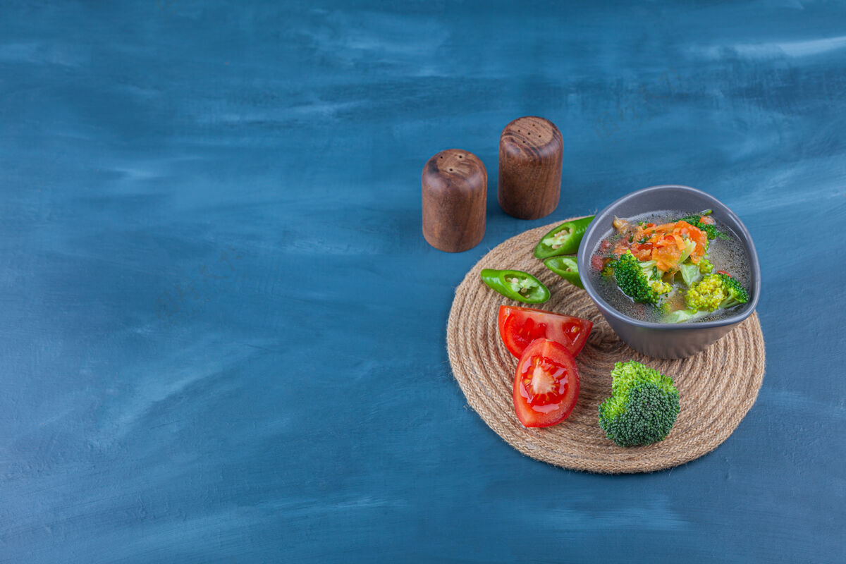 肉碗里的鸡汤和三脚架上的蔬菜片 在蓝色的桌子上生的营养有机